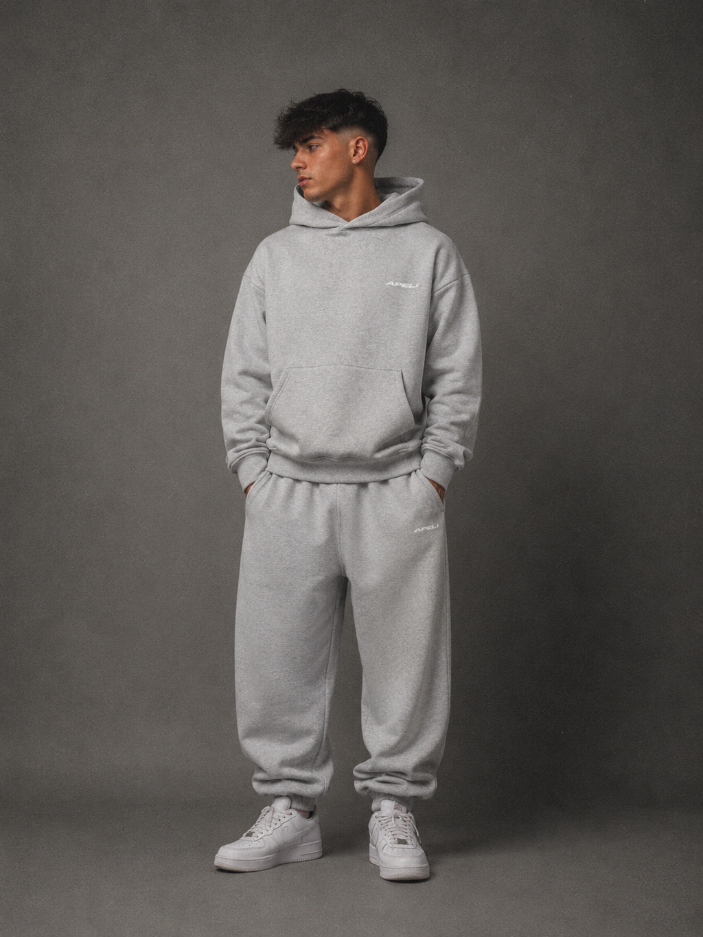 Person wearing a gray hoodie and pants set against a gray background