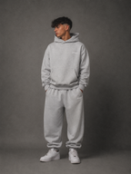 Person wearing a gray hoodie and pants set against a gray background